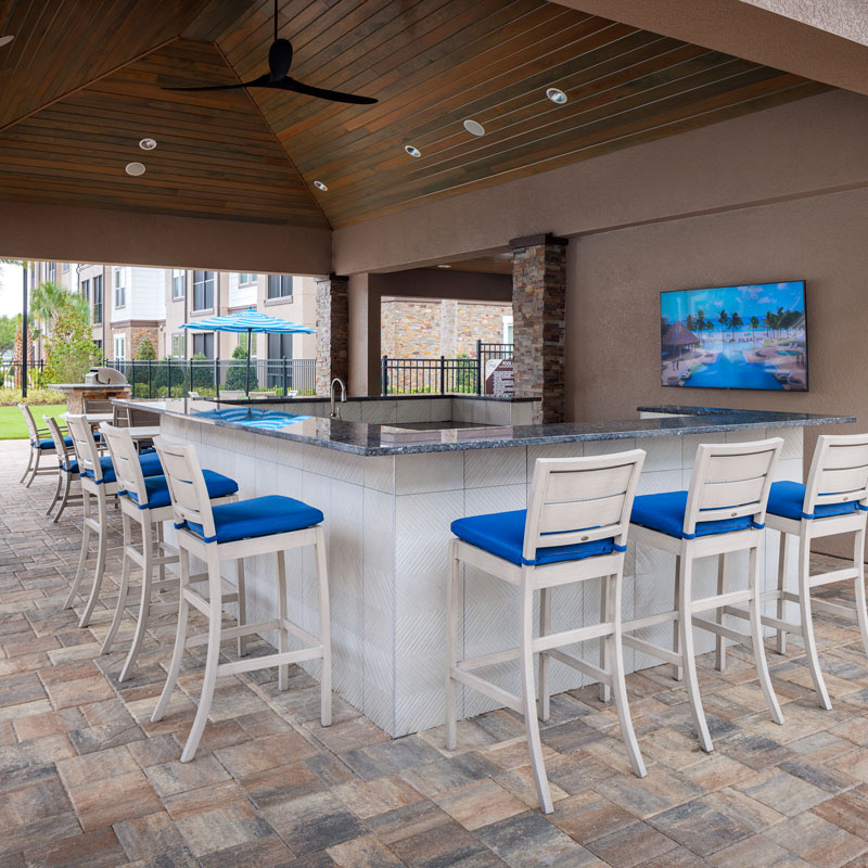 large bar with bar stools on a stone patio with a wooden roof overhang
