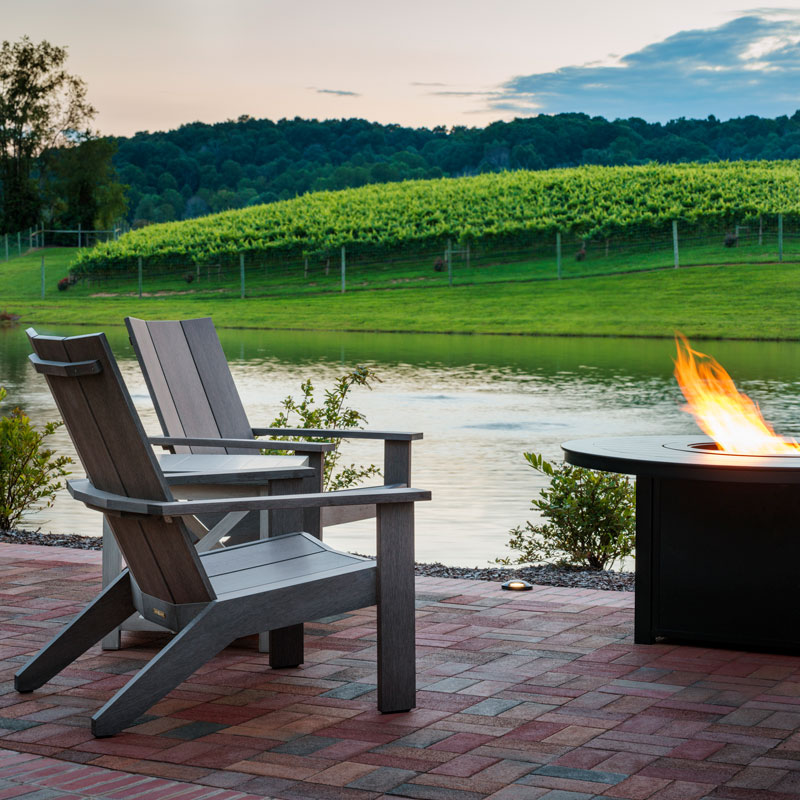 two wooden chairs with a lit fire pit by water